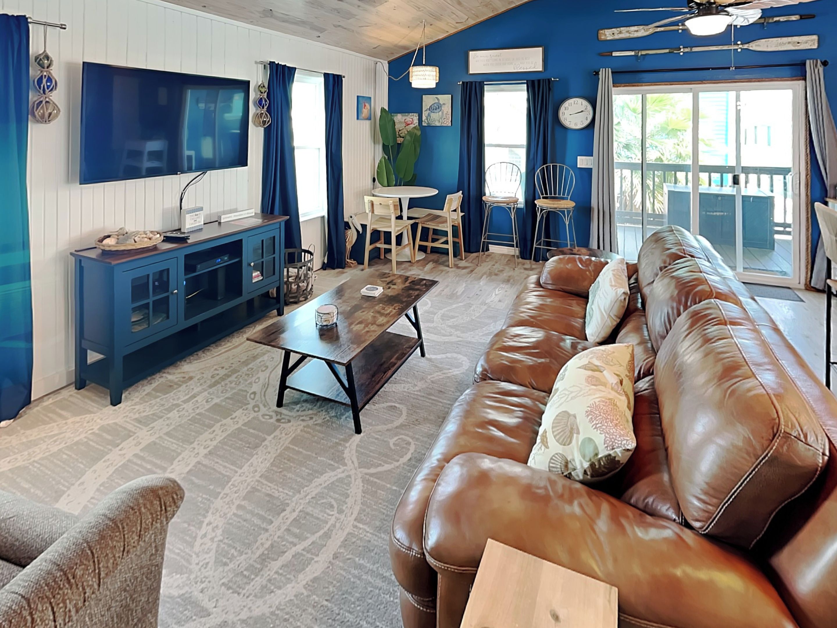 A living room with a brown leather sofa, a wooden coffee table, a blue cabinet, and a TV mounted on the wall.
