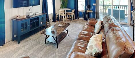 A living room with a brown leather sofa, a wooden coffee table, a blue cabinet, and a TV mounted on the wall.