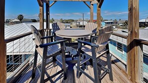 A wooden deck with a round table and chairs, overlooking a residential area with houses and a clear sky. - Sand Piper by Miss Kitty’s (Rockport)