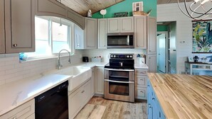 A modern kitchen with white cabinetry, a stainless steel oven, a microwave, and a dishwasher. - Sand Piper by Miss Kitty’s (Rockport)