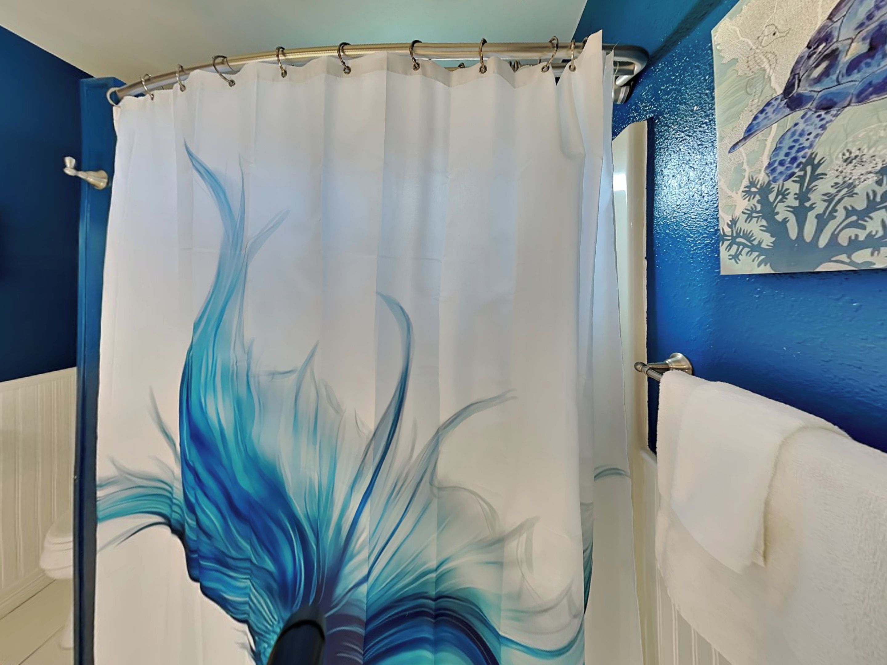 Een badkamer met een blauwe wand, een witte douchegordijn met een blauw abstract patroon, en een witte handdoekhouder.