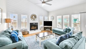 A spacious living room with a fireplace, a large flat-screen TV, and a ceiling fan. - The Salty Sandpiper by Silver Sands Vacation Rentals (Port Aransas)
