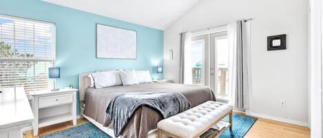 A bedroom with a bed, a bench, a desk, and a window.