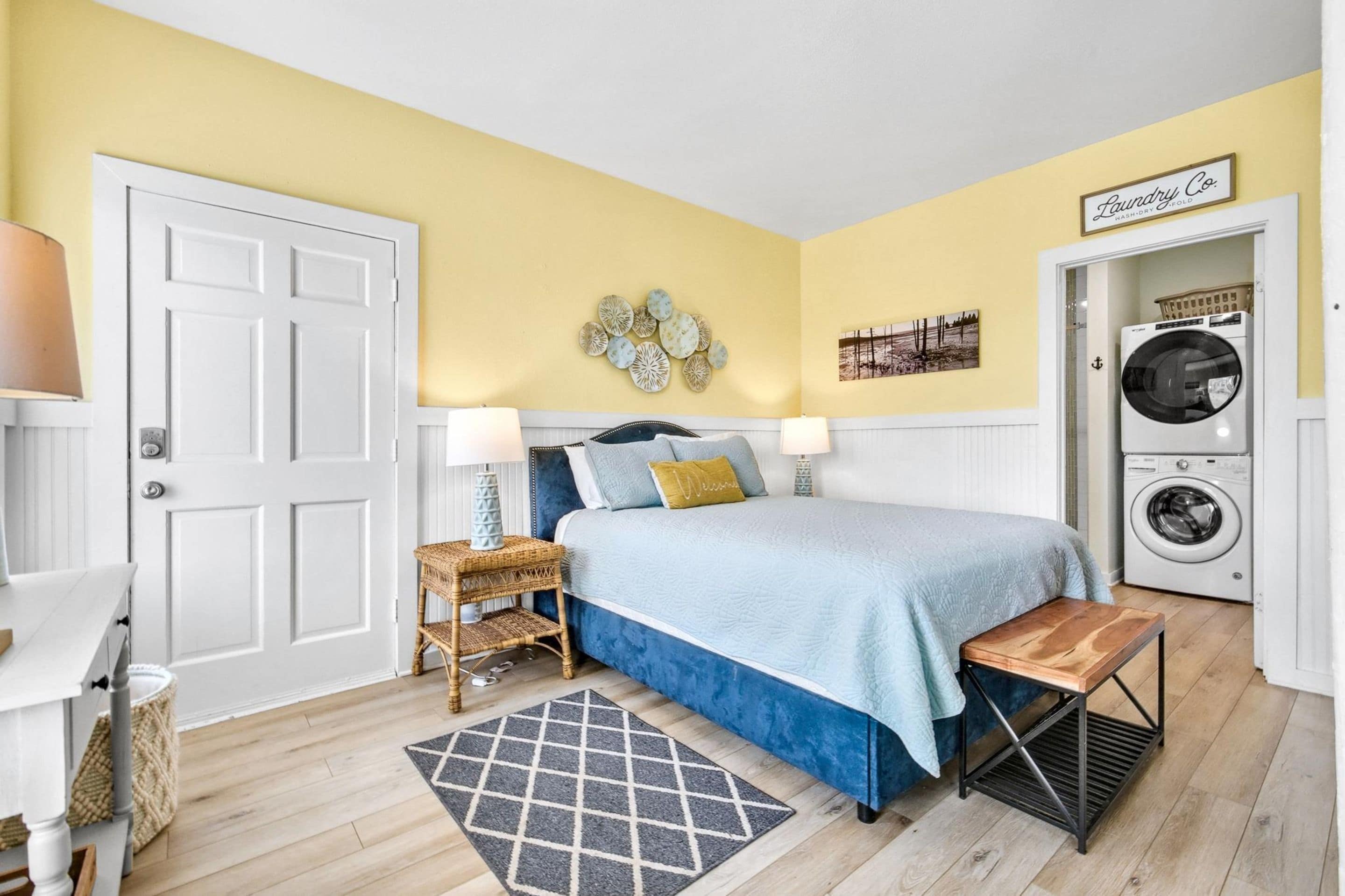 A bedroom with a bed, bedside tables, a washing machine, and a laundry sign.