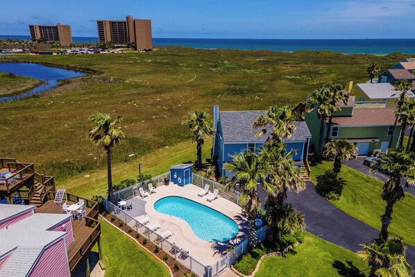 A resort with a swimming pool, palm trees, and a view of the ocean. - The Salty Sandpiper by Silver Sands Vacation Rentals (Port Aransas)
