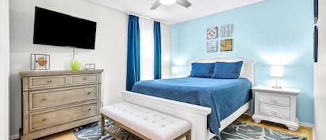 Un dormitorio con cama, cómoda, banco, televisor y ventilador de techo.