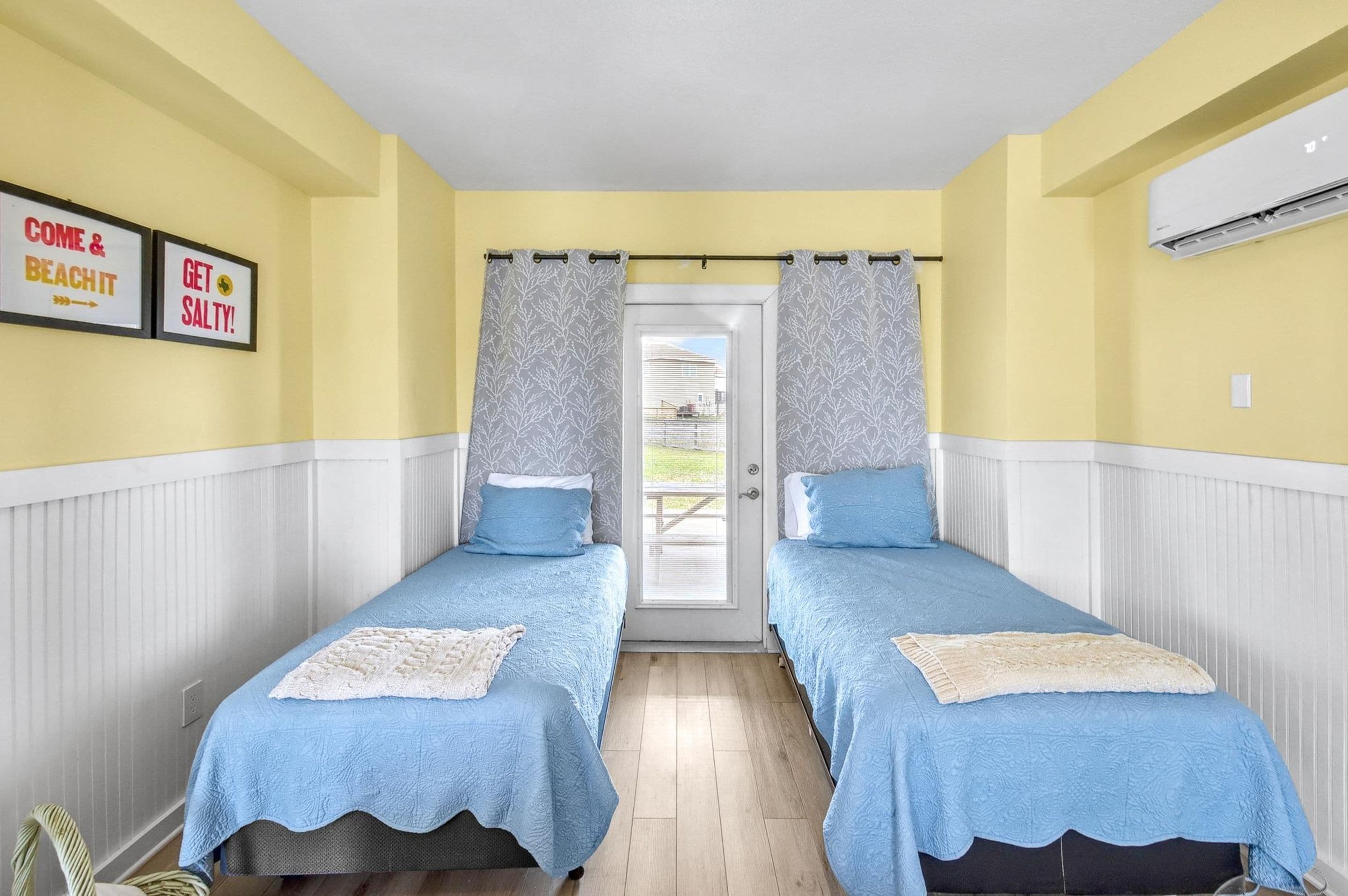 A room with two beds, a door leading outside, and a wall-mounted air conditioner.