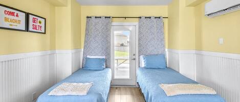 A room with two beds, a door leading outside, and a wall-mounted air conditioner.