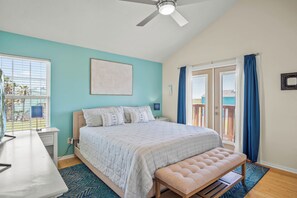 A bedroom with a bed, a bench, a desk, and a ceiling fan. - The Salty Sandpiper by Silver Sands Vacation Rentals (Port Aransas)