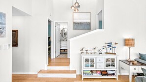A spacious living area with a staircase, a white console table with decorative items, and a view into the kitchen. - The Salty Sandpiper by Silver Sands Vacation Rentals (Port Aransas)