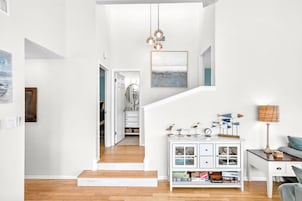 Un vaste espace de vie comprenant un escalier, une console blanche agrémentée d’objets décoratifs et donnant sur la cuisine.
