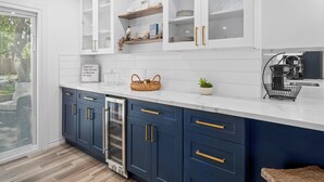 A modern kitchen with white upper cabinets, blue lower cabinets, and a marble countertop. - Reel Blessing by Miss Kitty’s (Rockport)
