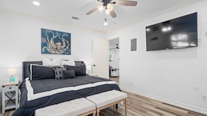 Une chambre à coucher avec un lit, un banc, un ventilateur de plafond, une télévision et un tableau accroché au mur.
