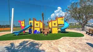 Ein Spielplatz mit Rutschen und Klettergerüsten, umgeben von einem Zaun und einem Baum.