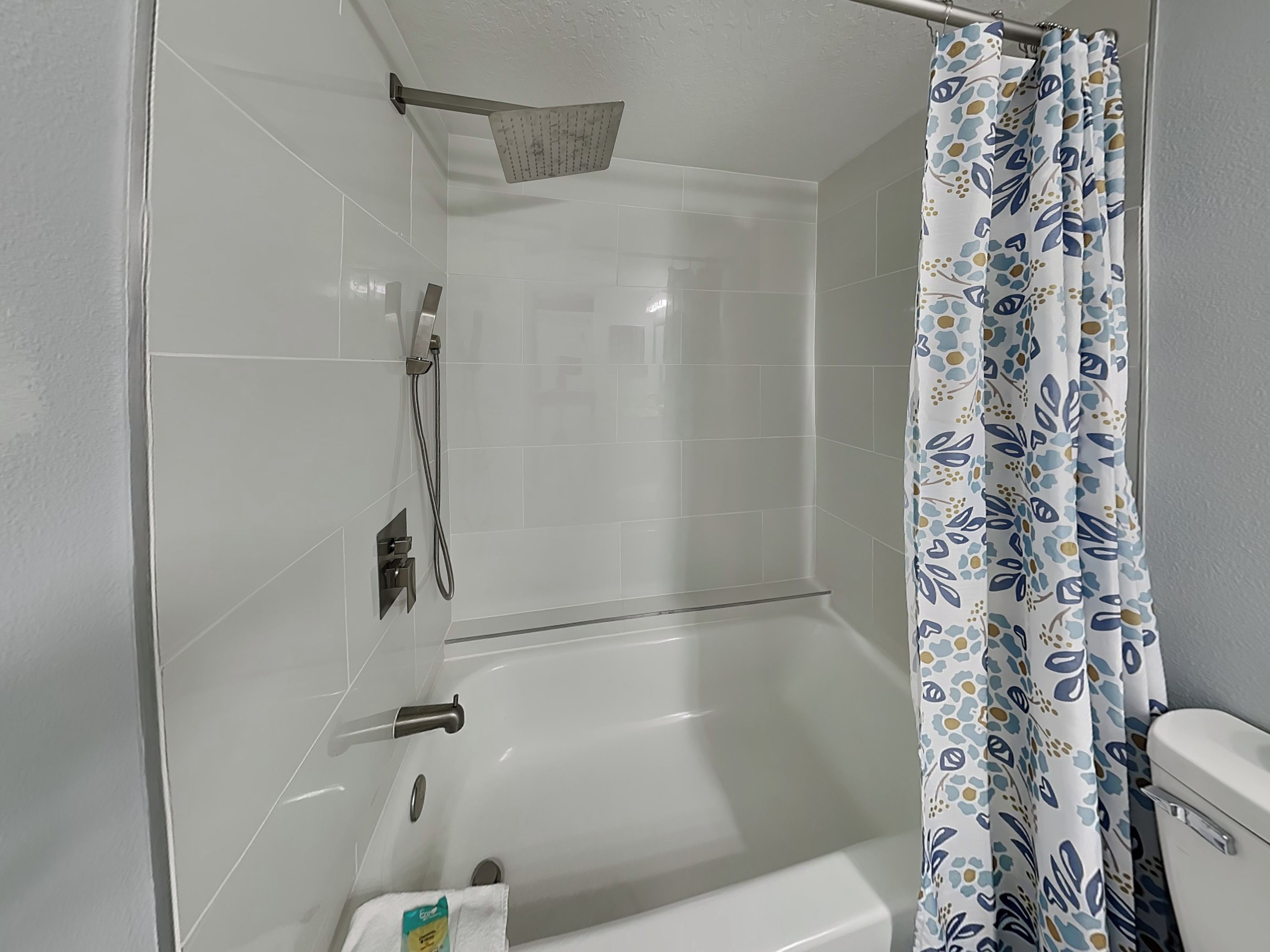Et badeværelse med bruser, toilet og badekar.