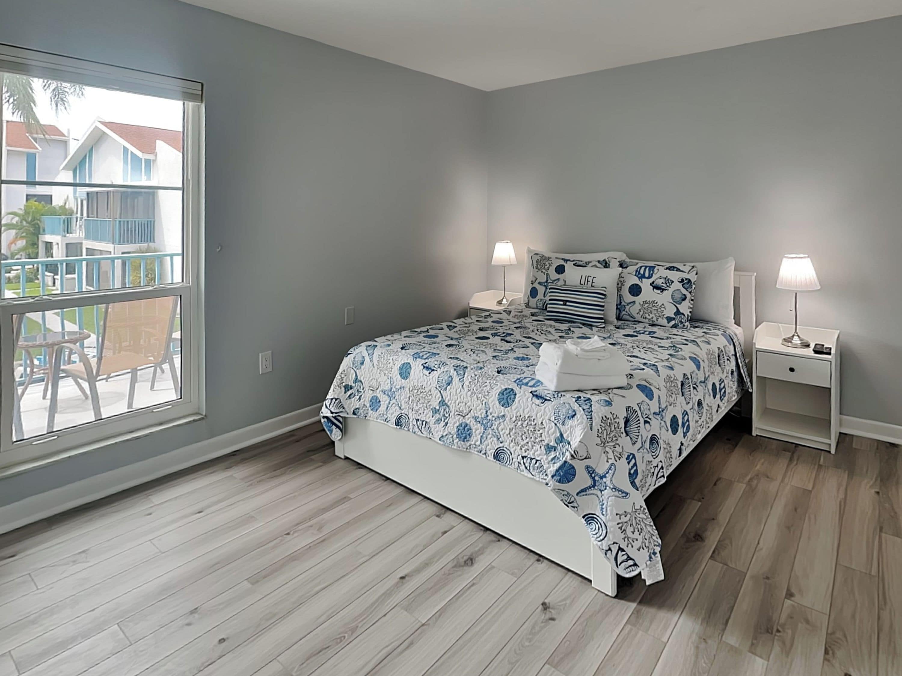 A bedroom with a bed, two bedside tables, a window, and a view of the outside.