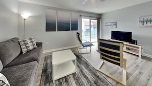 Ein modernes Wohnzimmer mit einem grauen Sofa, einem weißen Couchtisch, einer TV-Konsole und einem Deckenventilator.