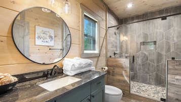 A bathroom with a wooden interior, a round mirror, a sink with a marble countertop, and a shower with hexagonal tiles.