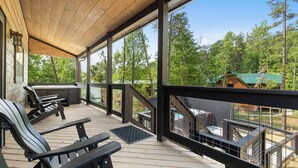 A wooden deck with outdoor seating and a view of a cabin in a forest.
