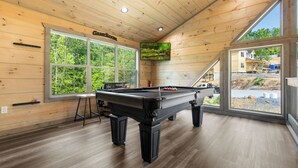 A pool table in a room with wooden walls and large windows.