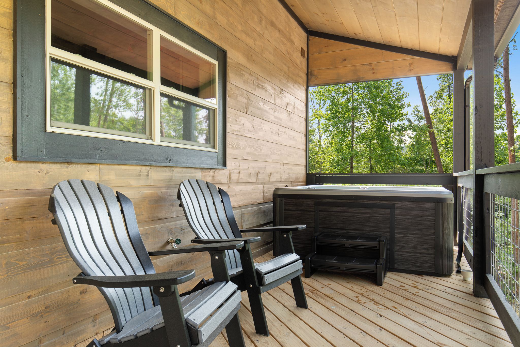 A wooden deck with Adirondack chairs and a hot tub.