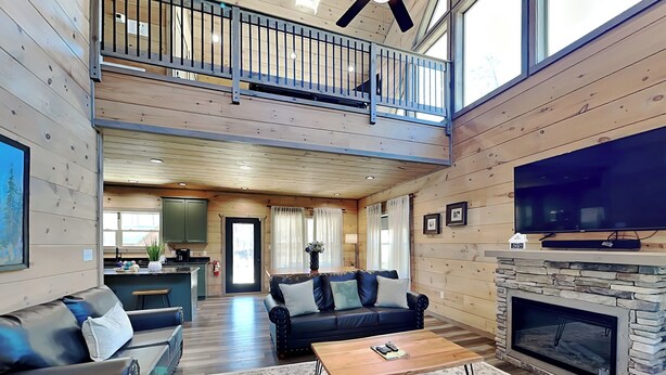 A spacious living room with a fireplace, a large TV, and a balcony.