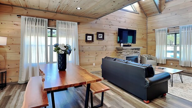A wooden cabin interior with a dining table, sofa, and fireplace. - Spool Time by Smoky Cove Resort (Sevierville)