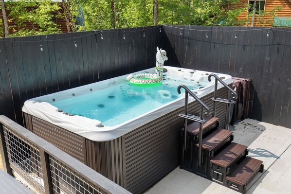A hot tub with steps and a decorative item in the water, surrounded by a wooden fence. - Spool Time by Smoky Cove Resort (Sevierville)
