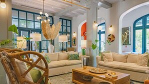 A spacious living room with two sofas, a coffee table, and a wicker chair. There are large windows with blue frames and a view of greenery outside. - Casa de los Sueños- 5 BR Home at Las Catalinas (Catalinas)