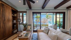 A spacious living room with a wooden bookshelf, a sofa, a coffee table with decorative items, and large windows offering a view of the outdoors. - Casa de los Sueños- 5 BR Home at Las Catalinas (Catalinas)