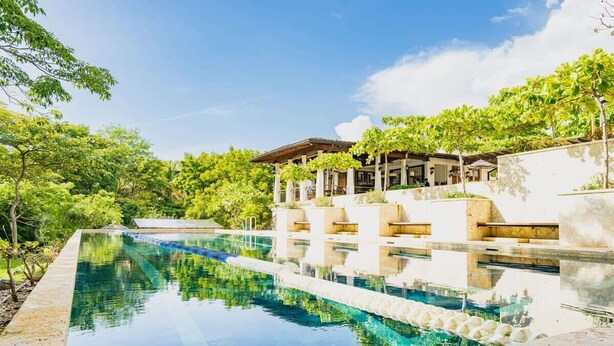 A swimming pool with a clear blue water, surrounded by lush greenery and a covered seating area with chairs. - Casa de los Sueños- 5 BR Home at Las Catalinas (Catalinas)