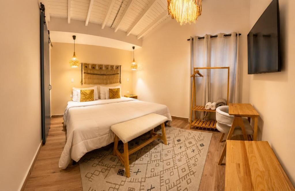 A hotel room with a bed, bedside table, bench, and a small wooden table.