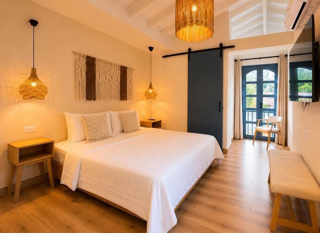 A bedroom with a bed, bedside tables, a bench, a hanging light fixture, and a sliding door leading to a balcony.