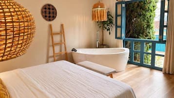 Ein Schlafzimmer mit einem großen Bett, einer Badewanne, einer Holzleiter und Blick durch eine offene Tür.
