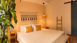 A bedroom with a bed, bedside tables, a hanging light fixture, a wall tapestry, and a wooden ladder.