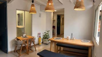 Um quarto com uma mesa de jantar de madeira, duas cadeiras, um banco e três luminárias pendentes de vime.