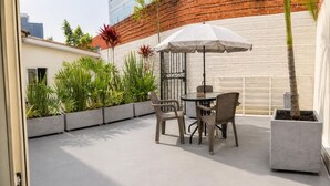 An outdoor patio with a table and chairs, surrounded by potted plants and a white wall.