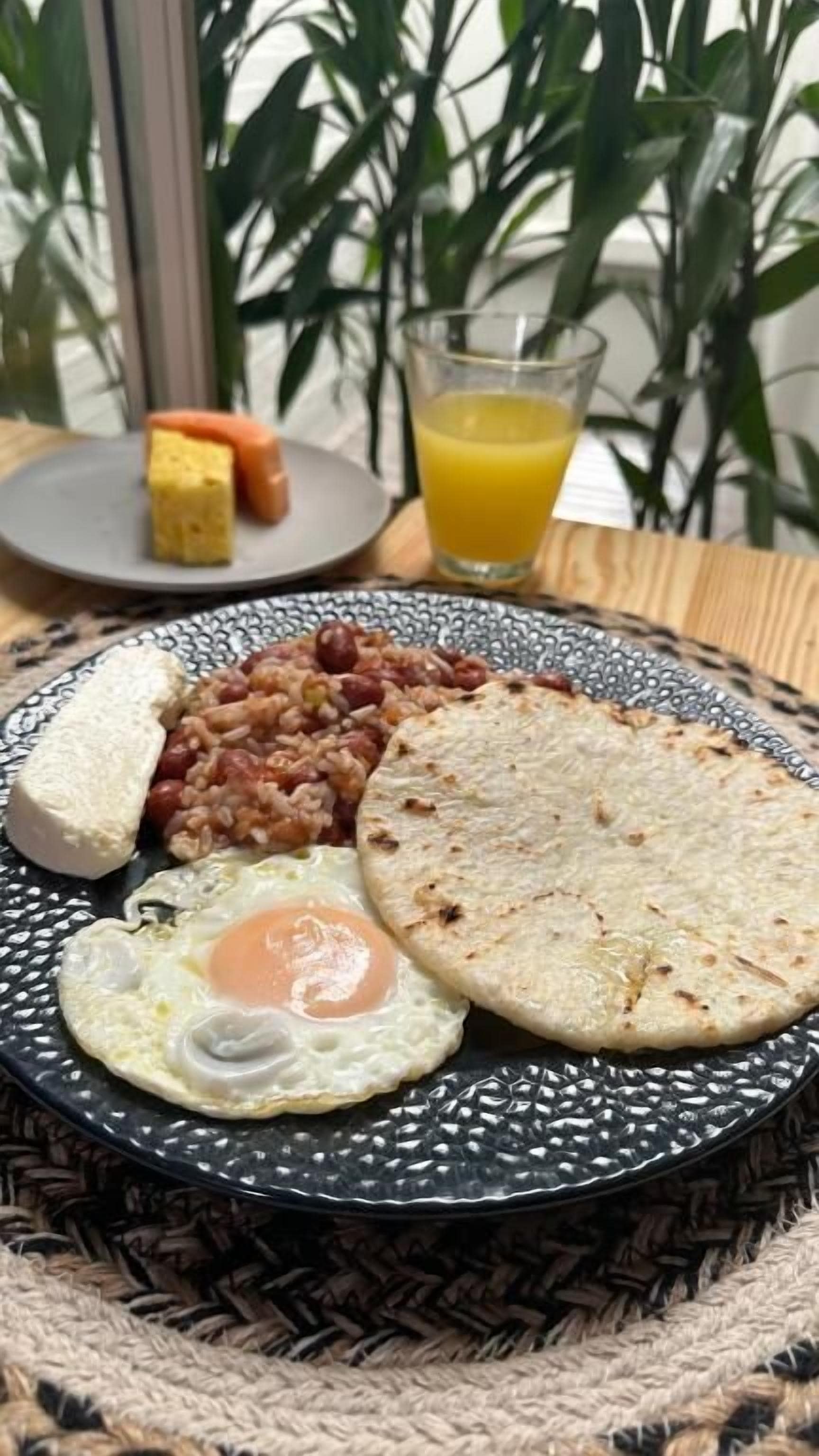 A breakfast plate with eggs, beans, bread, and a flatbread on a patterned plate.