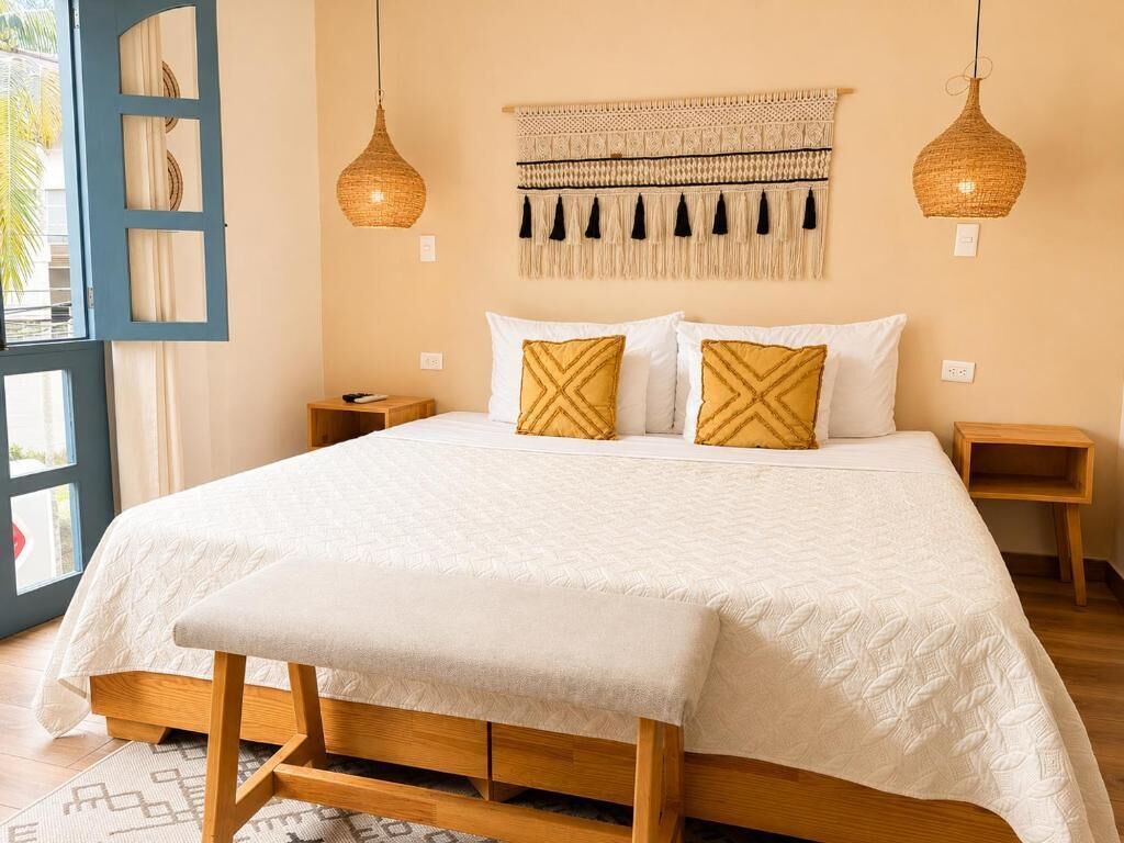 A bedroom with a bed, bedside tables, a wall tapestry, and hanging lamps.