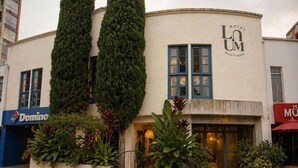 A building with a curved facade, two tall trees in front, and a sign for 'Hotel LUM Boutique'.