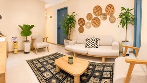 A living room with a sofa, two armchairs, a coffee table, and a patterned rug. There are two potted plants and a wall-mounted decorative item. - Luum Boutique Hotel (Medellín)