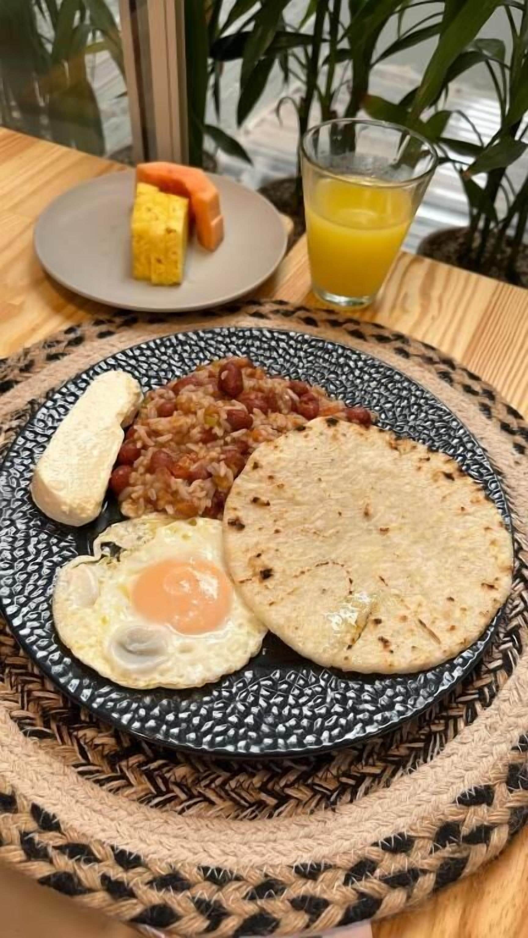 Un plato con un huevo frito, frijoles y una rebanada de pan, acompañado de un vaso de jugo de naranja.