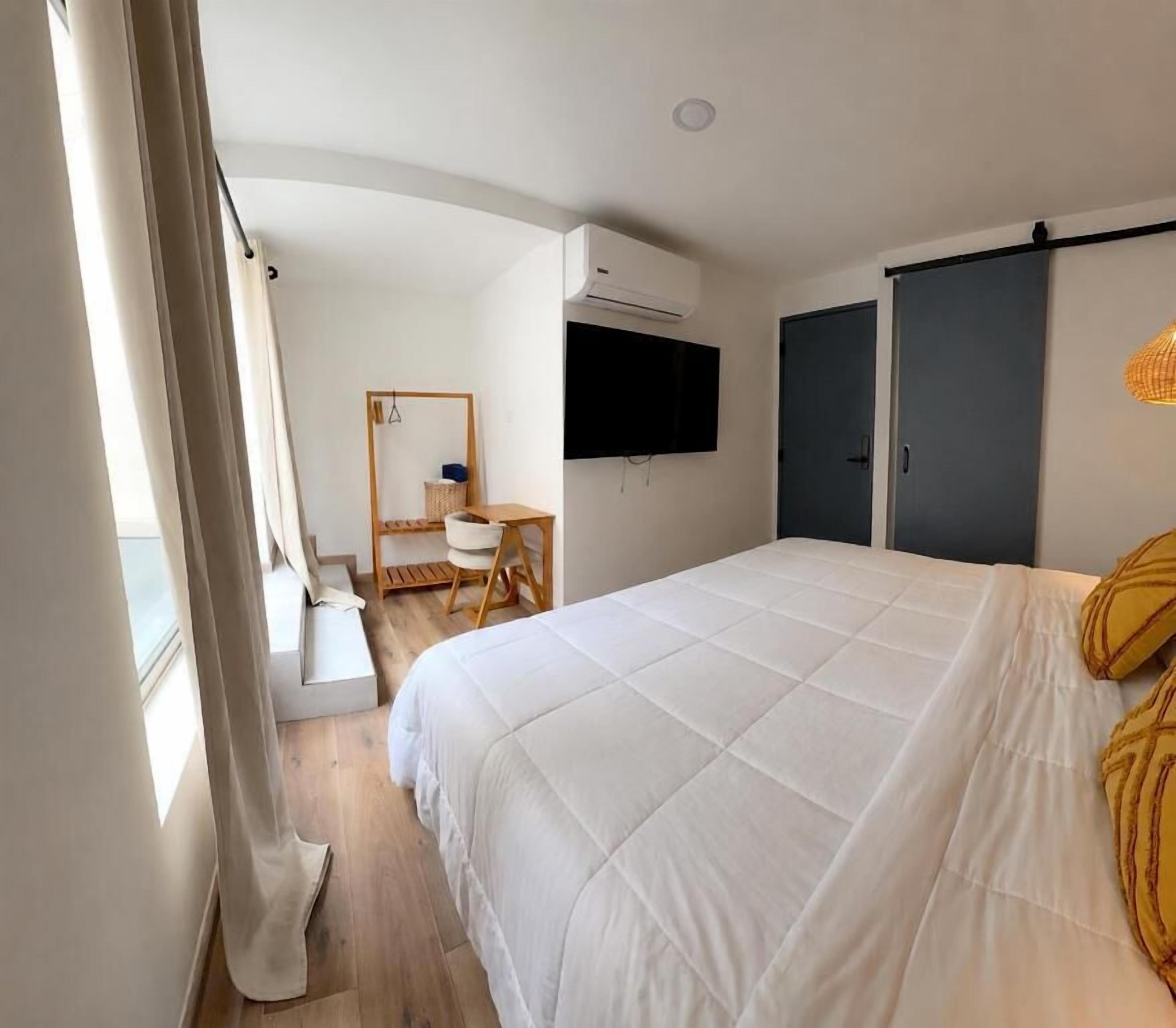 Un dormitorio con cama, escritorio, silla, televisor montado en la pared y puerta corredera.