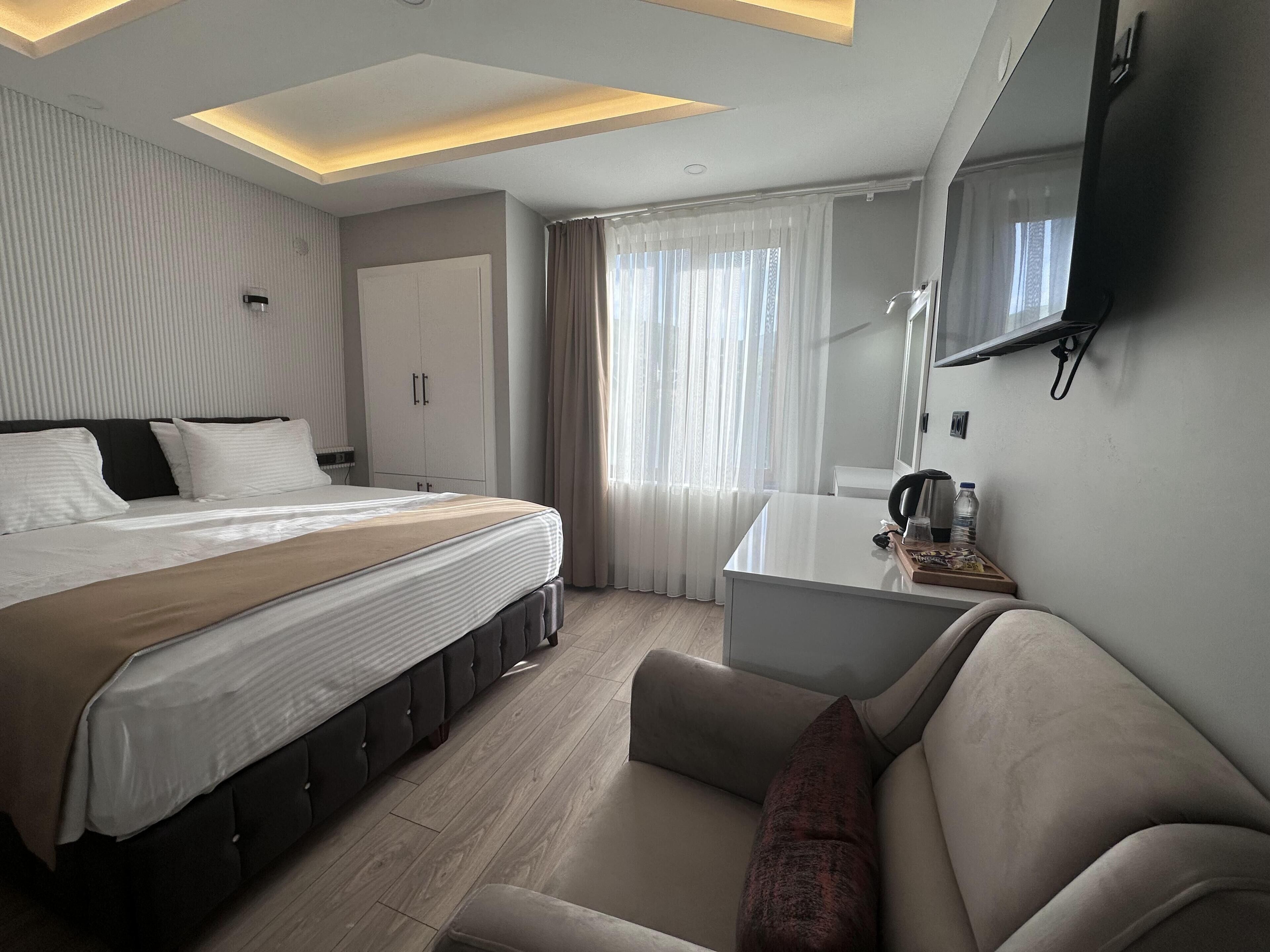 A modern hotel room with a large bed, a desk, a sofa, and a TV mounted on the wall.
