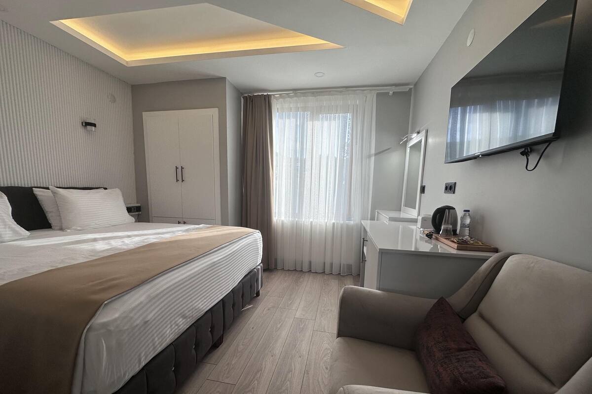 A modern hotel room with a large bed, a desk, a chair, and a TV mounted on the wall.