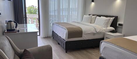 Een moderne hotelkamer met een bed, een bank, een klein tafeltje met een waterkoker en uitzicht op het omliggende landschap door grote ramen.