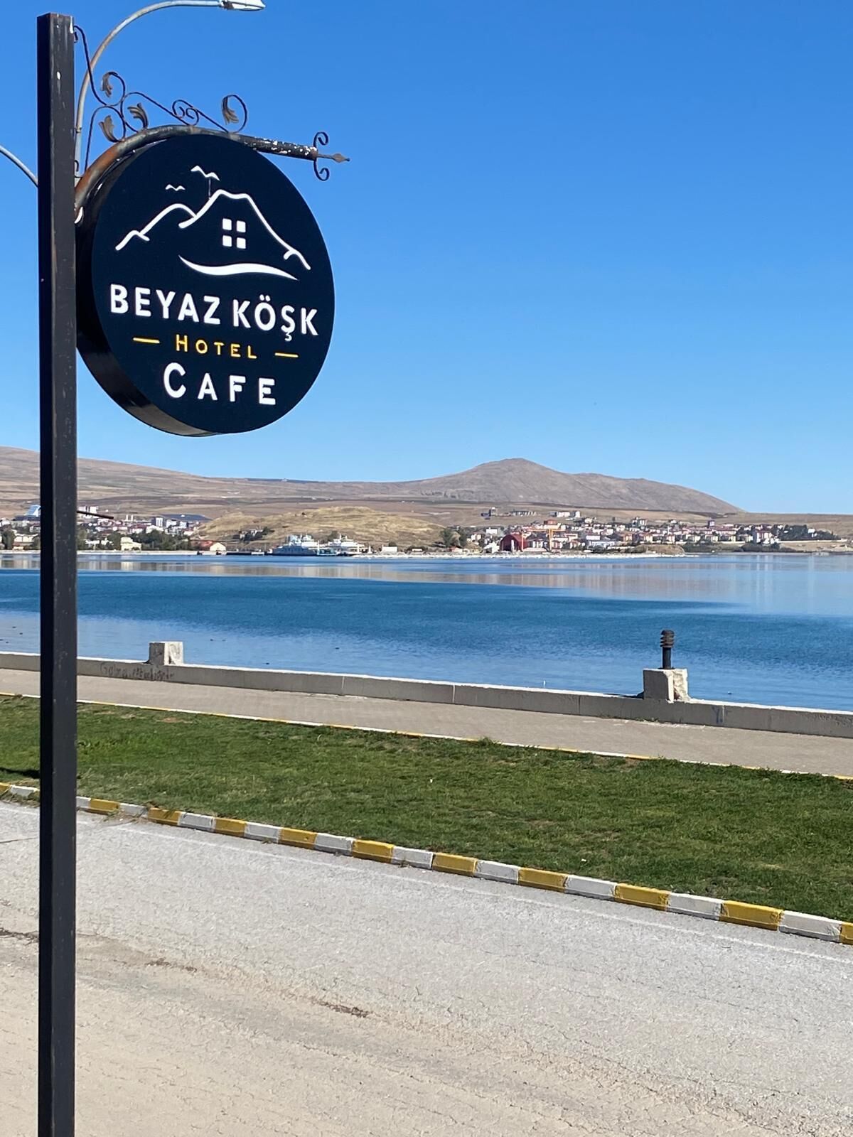 Señal para el Hotel Cafe Beyaz Koks, con vista a un lago y montañas al fondo.