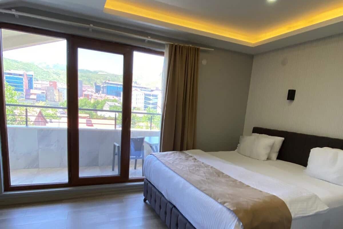 A hotel room with a large bed, a balcony with a view of buildings, and a sliding glass door.