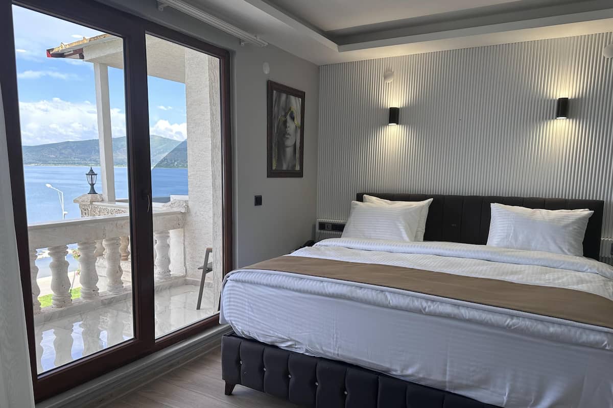A bedroom with a large bed, a view of the sea, and a balcony with a railing.