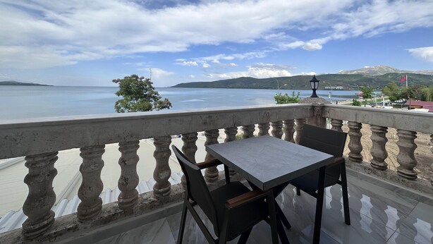 A balcony with a table and chairs overlooking a lake with mountains in the background. - Beyaz Köşk Hotel & Cafe (Tatvan)